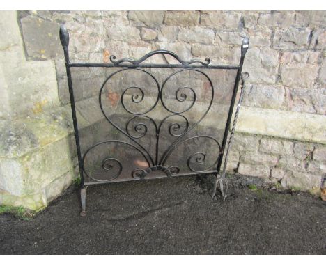 A heavy gauge iron work firescreen with open scrollwork and mesh panel, together with a blacksmith made fire tool, the screen