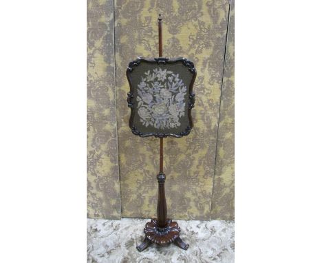 A 19th century mahogany pole screen with shield shaped tapestry panel raised on a partially turned pillar, petal platform and