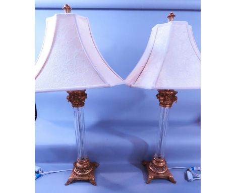 A pair of Neoclassical style glass Corinthian column table lamps with gold metal scrolled caps on gold bases with swept suppo