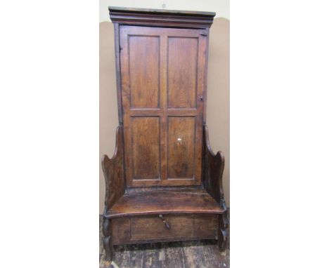 An 18th century elm bacon settle, the raised back enclosed by a quarter panelled door, within shaped and splayed supports, wi