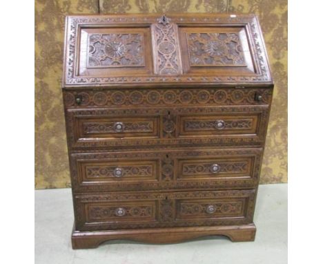 A Victorian oak bureau the front elevation with all over carved floral  decoration, the fall front enclosing fitted interior 