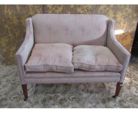 An Edwardian two seat sofa with upholstered finish, loose seat cushions, down swept slab arms and square tapered supports wit