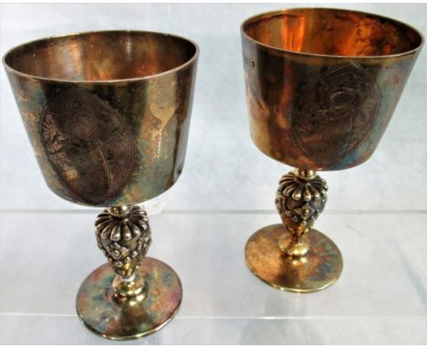 A pair of silver goblets, each bowl bearing a heraldic motif with an otter and fish engraved above, the stems having lion hea