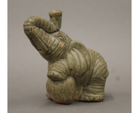 A green-glazed pottery model of an elephant with trunk raised and one foreleg on a ball. 12 cm high.