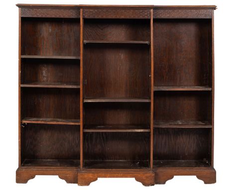 An Edwardian oak low open breakfront bookcase; with a moulded top and blind fret carved geometric frieze, fitted with adjusta