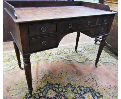A mid-19th century mahogany writing desk with five frieze drawers to a central kneehole, raised on turned supports with brass