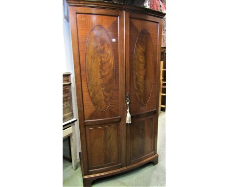 An Edwardian mahogany bow fronted wardrobe in the Georgian style, enclosed by a pair of full length twin panelled doors with 