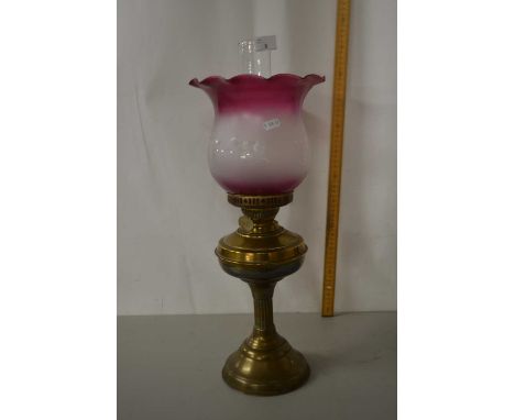 A brass based oil lamp with cranberry tinted shade