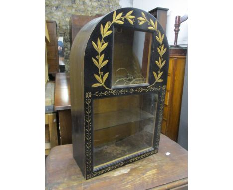 An early 20th century black and gold painted, arched topped hanging display cabinet with twin glazed panels and a shelf