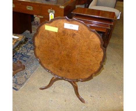 A C20th walnut tilt top pie-crust low table raised on tripod base