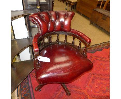 A mid C20th mahogany swivel captain chairs upholstered in red button leather raised on castors