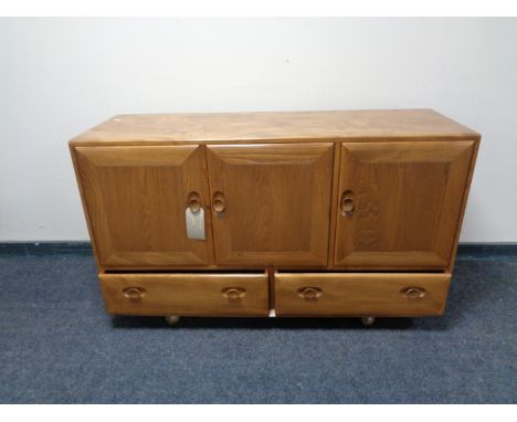 An Ercol elm and beech triple door sideboard fitted two drawer beneath on castors 