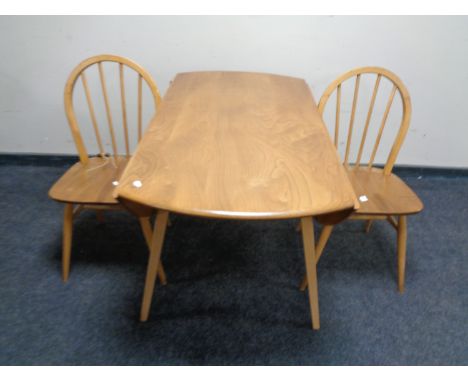 An Ercol elm and beech circular drop leaf table and two spindle back chairs 