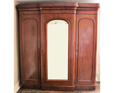 A Victorian mahogany breakfront wardrobe, with arched mirrored door flanked by two panelled doors, the interior with an arran