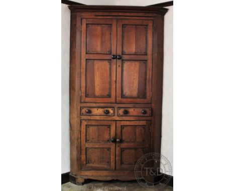 An impressive George III oak corner cabinet, the two panelled cupboard doors enclosing shelves above two drawers and two furt