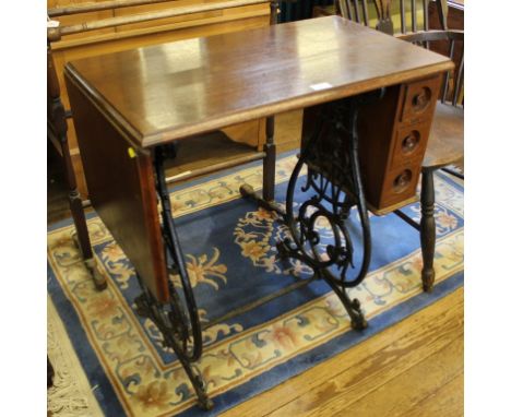 An early 20th century converted sewing machine table with shaped top, single drop leaf on a black-painted wrought iron frame,