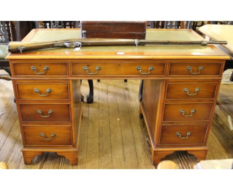 A Georgian-style yew wood pedestal desk with shaped top, green leather inset, one long and eight short drawers with brass dro