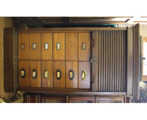 An early 20th century oak stained office reference bureau with shaped cornice, rolled down tambour-style front, sixteen small