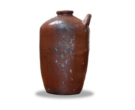 A water jug in terracotta fabrication and light  brown coloration. The vase has one rounded handle  near the spout at the top