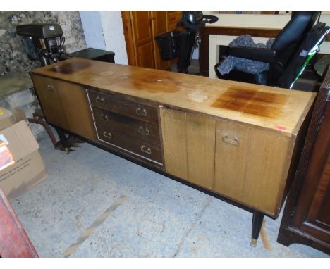 A retro G-Plan teak sideboard with three central drawers flanked by cupboard doors on tapering legs and brass cups and castor