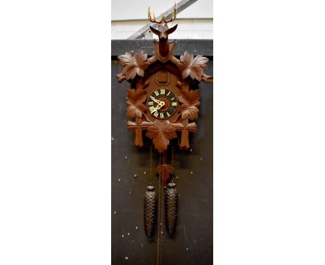A Swiss cuckoo clock, dial set with Roman numerals, case surmounted with a stags head and carved leaf decoration, fir cone we