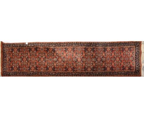 A terracotta ground hand-knotted Persian woollen runner with central panel of flora and fauna within a geometric border, 288 