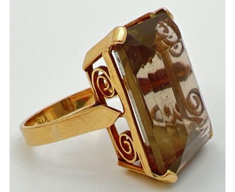 An 18K gold cocktail ring set with a large emerald cut smoked quartz stone. In claw set mount with pierced scroll design to s