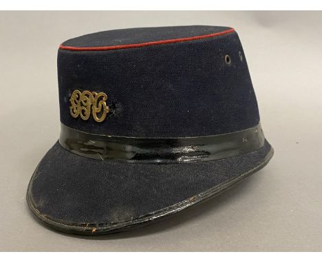 A GEORGE V POST OFFICE CAP. A black fabric 'Shako' style GPO workers hat with oval top with red beading, the front with initi