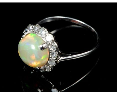 Opal and diamond cluster ring with a central opal cabochon surrounded by a border of single cut diamonds, on a precious white