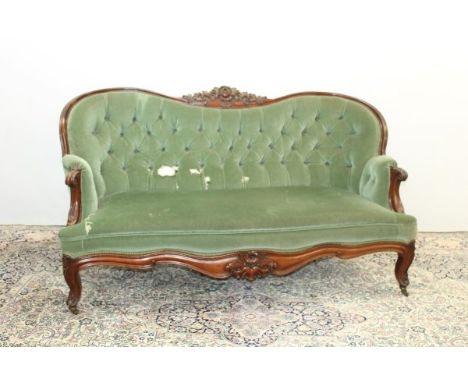 Good quality Victorian mahogany framed camel back sofa with floral carved cresting, buttoned green velvet upholstery, on carv