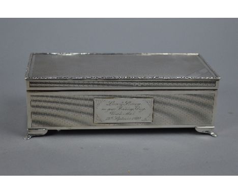 AN ELIZABETH II RECTANGULAR SILVER TABLE TOP CIGARETTE BOX, foliate cast rim, engine turned decoration, the front with presen