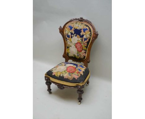 A VICTORIAN FANCY CARVED WALNUT FRAMED NURSING STYLE CHAIR, with floral wool work back and seat pad, supported on twin fancy 