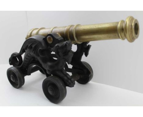 A MODEL GUN CANNON with ring turned brass barrel, on a cast iron dragon decorated base with four wheels. the barrel length; 3