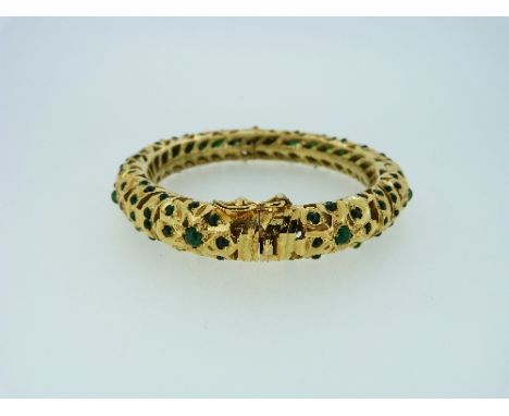 An attractive Indian style hinged Bangle, of ornate pierced design in gilt metal set various sized green glass stones. 
