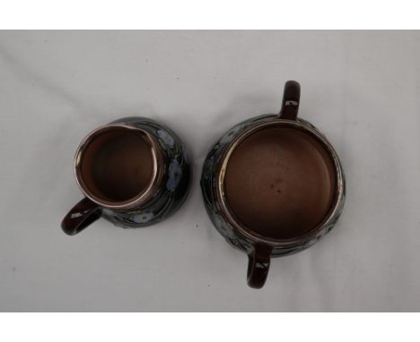 A Doulton Lambeth stoneware cream jug and twin handled sugar basin, moulded with flowers and leaves to a mottled ground, impr