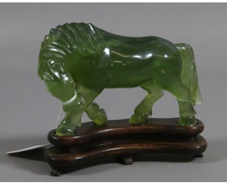 A Jade coloured hardstone model of a horse raised on a wooden plinth.