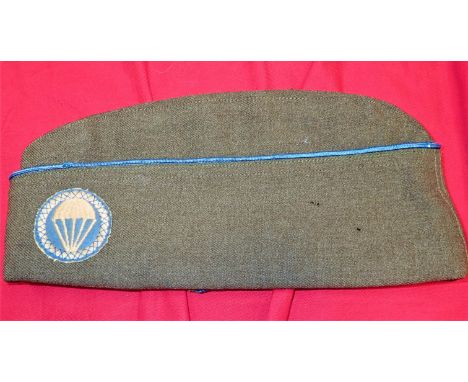 Green wool cap, blue-piped, showing wear, with cross-stitched paratroopers’ patch &amp; divisional enamel badge.