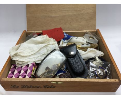 A cigar box containing enamel badges pen knifes cufflinks and other oddments.