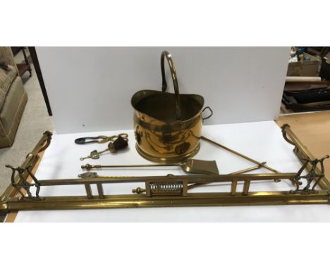 An early 20th Century brass fender, a set of three brass fire irons and other fire tools and a copper coal helmet