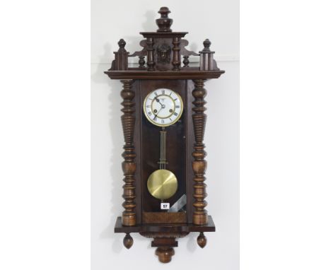 A Vienna-type wall clock having black roman numerals to the two-part white enamel dial, &amp; in a carved wooden case, 96cm h