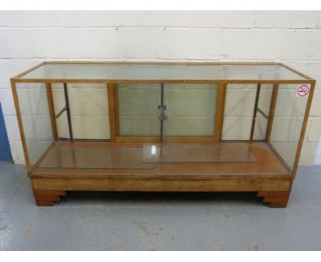 An Art Deco glazed oak haberdashery or shop fitting counter with glazed shelf and sliding doors raised on stepped feet