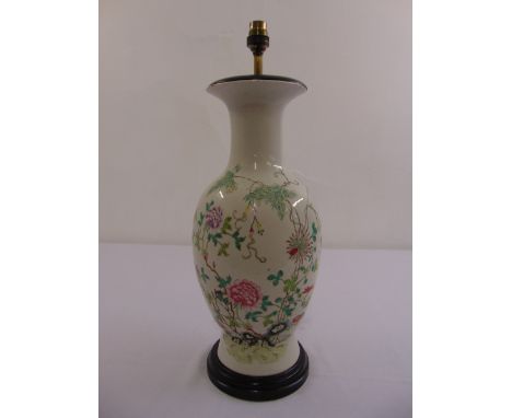 A Chinese baluster form lamp base decorated with flowers and leaves on a hardwood stand