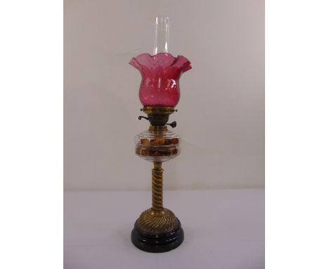 A cranberry glass oil lamp on brass column and raised circular base