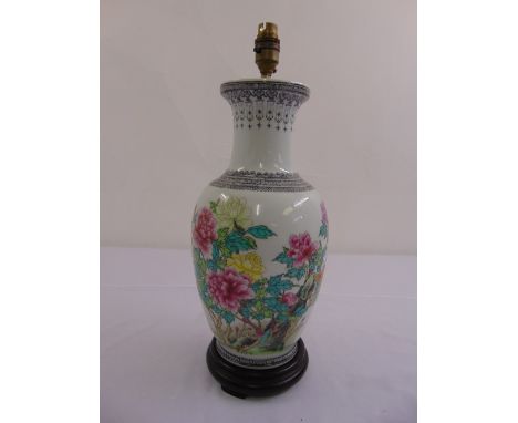 A Chinese ovoid lamp base decorated with flowers and leaves on a hardwood stand