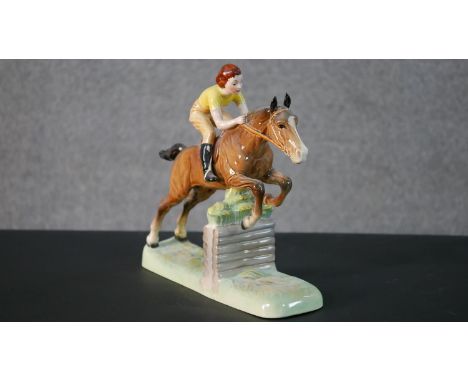 A Beswick hand painted ceramic model of a lady jockey in yellow shirt jumping a fence, makers mark to the base. H.25 W.27.5 D