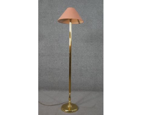 A brass standard lamp, with a salmon coloured shade, on a cylindrical reeded and turned stem with a circular base. H.158 Diam