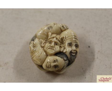 A carved bone Netsuke decorated with faces 