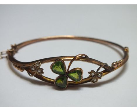 A 9CT GOLD SHAMROCK BANGLE, set with green peridot type stones with two further seed pearl set shamrocks, approx weight 5.2g,