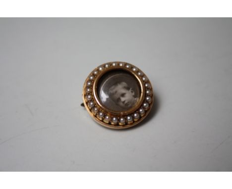 AN EDWARDIAN YELLOW METAL AND SEED PEARL LOCKET BROOCH, of circular form, with portrait photo to centre and seed pearl surrou