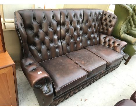 A BROWN LEATHER WING AND BUTTON BACK THREE SEATER SOFA 